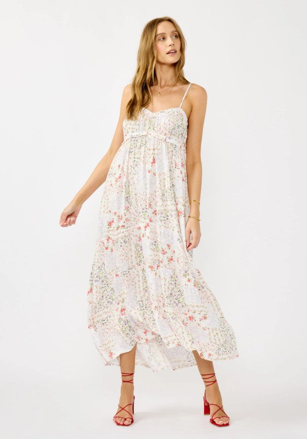 A woman modeling a white spaghetti-strap midi dress with a pink and green floral print, paired with red strappy high-heeled sandals, against a plain white studio background.